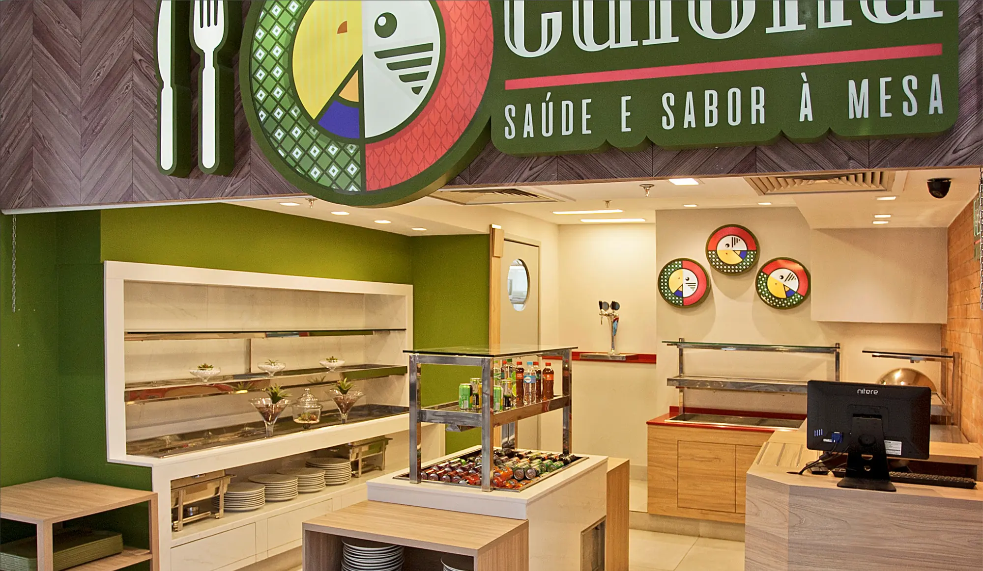 Restaurante Caiena com a marca na parede de tijolos, balcão de buffet e parede verde